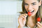 Young woman biting into a radish while holding another, smiling at camera, head and shoulders