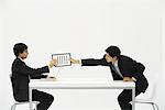 Two business associates sitting face to face at desk, one hand document to the other