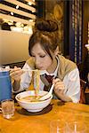 Young female eating bowl of ramen noodles in restaurant