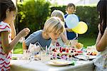 Boy blowing candles on birthday cake at outdoor birthday party