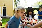 Boy blowing out candles on birthday cake at outdoor birthday party