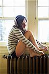 Woman sitting on Radiator by Window