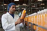 Worker examining orange juice bottle at bottling plant