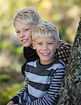 Portrait of two blonde boys leaning against tree trunk