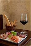 Dish of cold pork meats ,bread sticks and a glass of red wine on a table in a restaurant