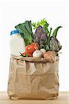 Vegetables and a bottle of milk in a brown paper bag