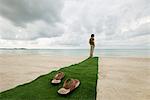 L'homme debout à la fin du tapis sur la plage, sandales au premier plan