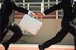 Businessmen running in relay race, handing off briefcase