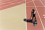 Woman crouched in starting position on running track, rear view