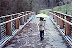 Girl walking on bridge with umbrella, rear view