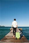 Man pulling luggage walking towards end of pier, rear view