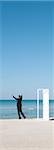 Businessman standing on beach looking at ocean with arms raised