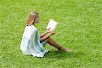 Young woman sitting on grass reading book