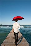 Man walking on pier with red umbrella, rear view