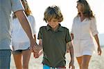 Boy walking on beach with family, holding father's hand