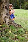 Trois enfants souriants derrière le tronc de l'arbre, Munich, Bavière, Allemagne