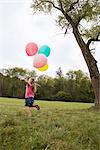 Girl running in meadow with balloons, Munich, Bavaria, Germany