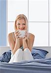 Woman in bed drinking tea from large cup