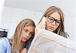 Mother reading newspaper and phoning with daughter by her side