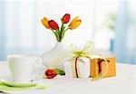 Two gifts, tulips and cup of coffee on table