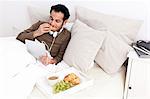 Mann mit Tablet-PC im Bett Essen