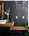 Salle de bain avec mur gris foncé orné miroir au cadre doré, lavabo et douche double avec banquette. Architectes : Hilit