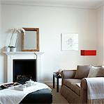 Orchid on fireplace of living room with sofa and ottoman footstool, UK.