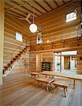 Wooden table and stools in centre of wood panelled room with high ceiling and staircase to upper floor