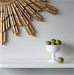 White bowl of greengages on ledge below gilt wall decoration