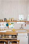 Kitchenware on shelf above sink set in wooden worktop in country style kitchen with wooden walls