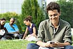 Young man text messaging with cell phone, group of people in background