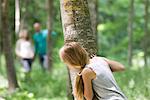 Girl hiking behind tree in woods