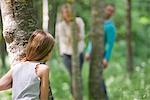 Girl playing hide and seek with parents in woods, rear view