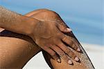 Woman rubbing sand off legs at the beach, cropped