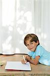 Boy lying on ground, drawing in notebook