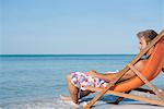 Young man reclining in deckchair looking at ocean, side view