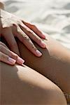 Woman touching bare legs at the beach, cropped