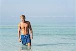 Barechested young man standing knee deep in water, portrait