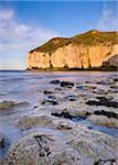 Smooth polished rocks on the shore at Thornwick Bay, looking towards the golden cliffs of Flamborough, Yorkshire, England, United Kingdom, Europe