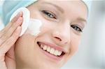 Young Woman face using a cleansing cotton on her cheek, close-up (studio)