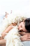 Naked woman with a white feather boa, lying on floor, shut eyes (studio)