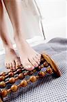 Young woman using wooden massager on her naked feet