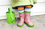 Little girl in boots, close-up, green watering can