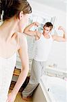Couple in bathroom, woman watching man flexing muscles