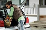 Young woman taking a shopping basket out of a car trunk