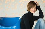 Young woman sitting on the floor, leaning against blue armchair, looking at the camera