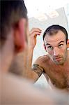 Tattooed man, barechested, looking in bathroom mirror