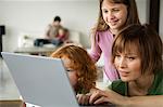 Woman and 2 little girls using laptop computer, man and child in the background