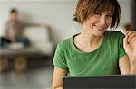 Smiling woman using laptop computer, man in the background