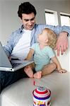 Man using laptop computer and little boy looking at each other, sitting on a sofa